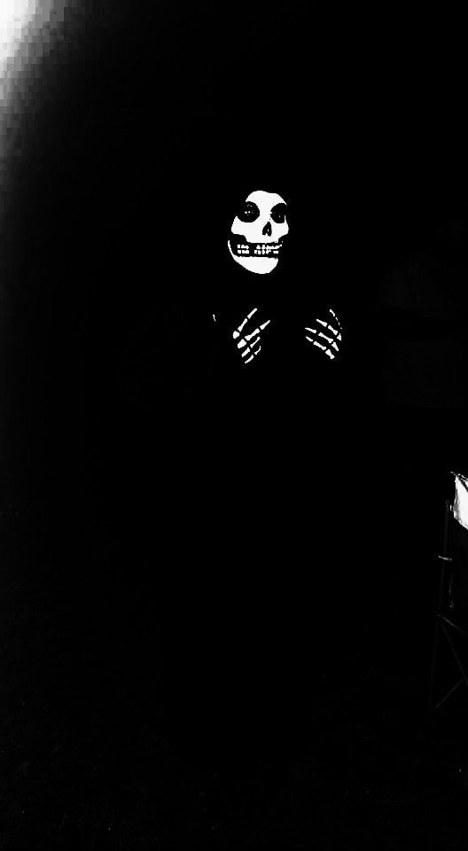 a black and white photo of a skeleton sitting in the dark with his arms crossed