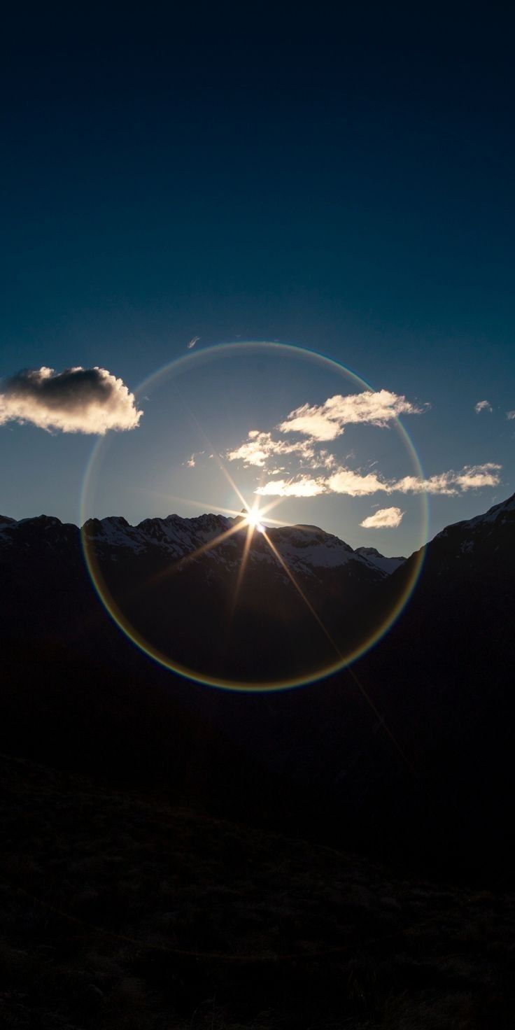 the sun shines brightly in front of mountains and clouds as it peeks through a circular lens
