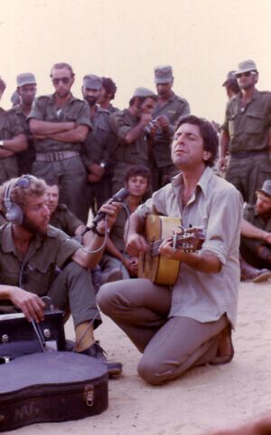 a group of men sitting on the ground with guitars and other people standing behind them