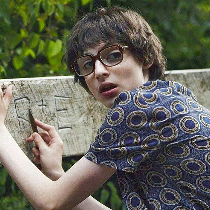 a person with glasses holding a cell phone in front of a wooden sign that says love is reddle