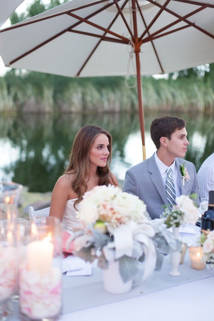 a man and woman sitting at a table with an umbrella over them, surrounded by candles