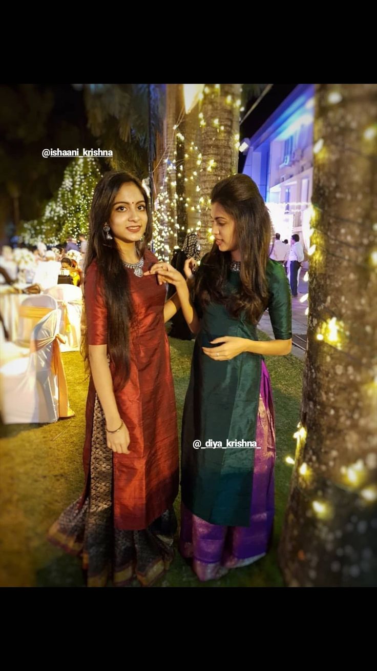 two women standing next to each other in front of a tree with lights on it