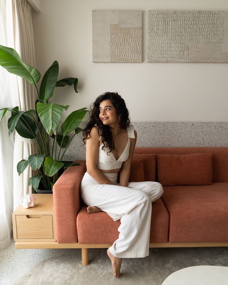 a woman sitting on top of a couch next to a plant