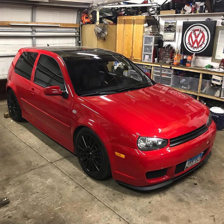 a red car parked in a garage next to a shelf filled with tools and other items