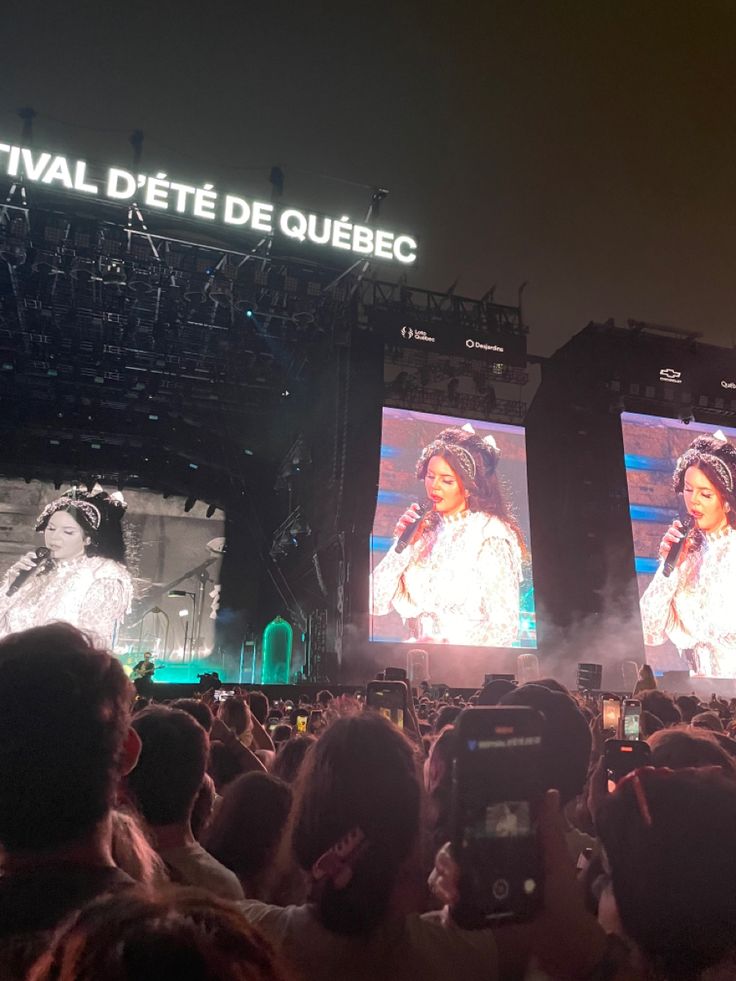 people are standing in front of two large screens at a concert with lights on them