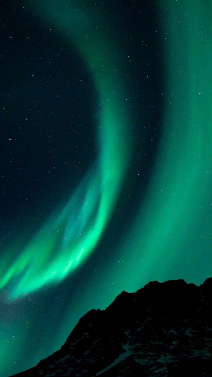 an aurora bore is seen in the night sky over mountains and snow covered hills with green lights