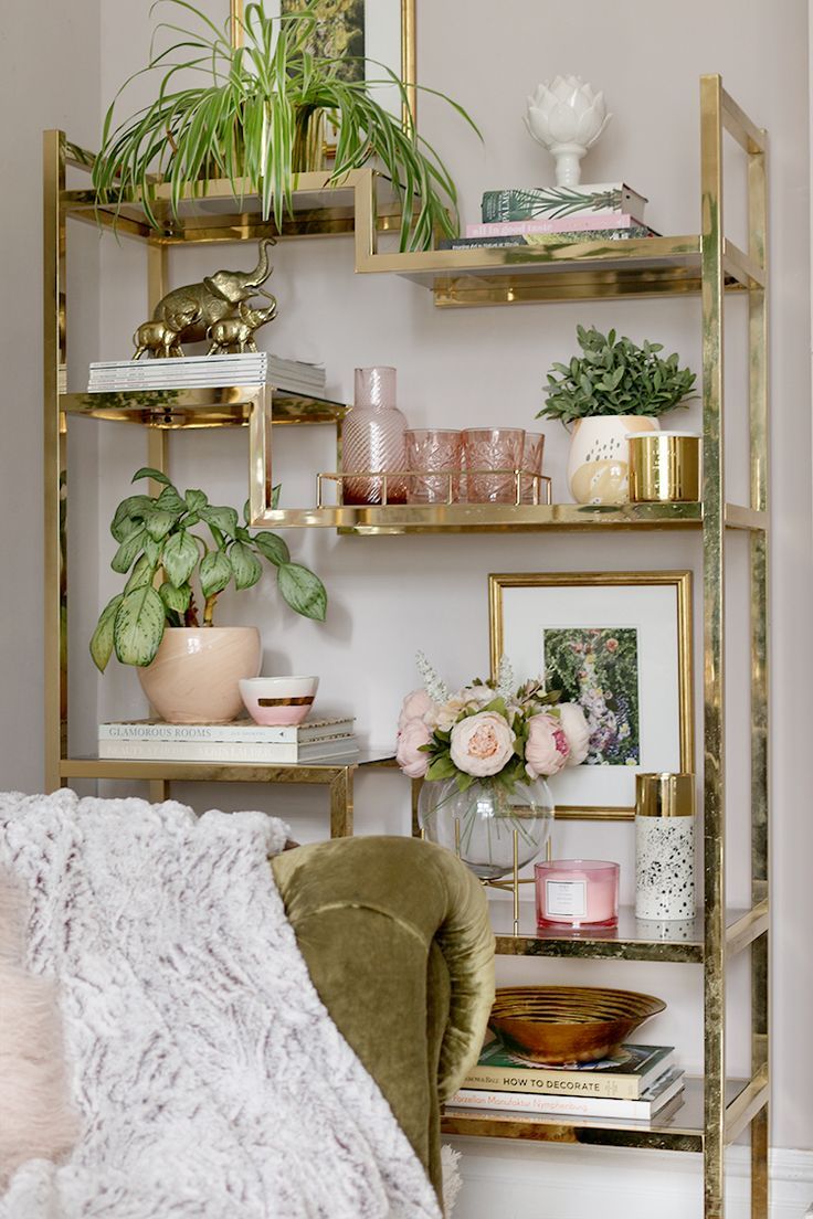 a living room filled with lots of plants and books on top of gold shelving