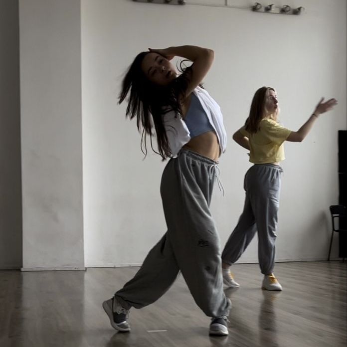 two young women are dancing in an empty room, one is wearing grey sweatpants and the other is yellow