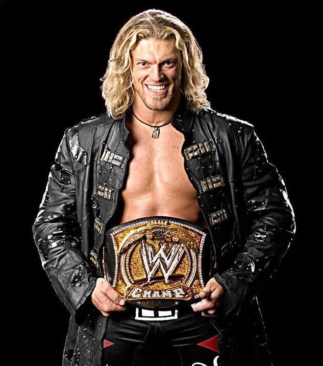 a man in leather jacket holding a wrestling belt with his hand on his hip and smiling at the camera