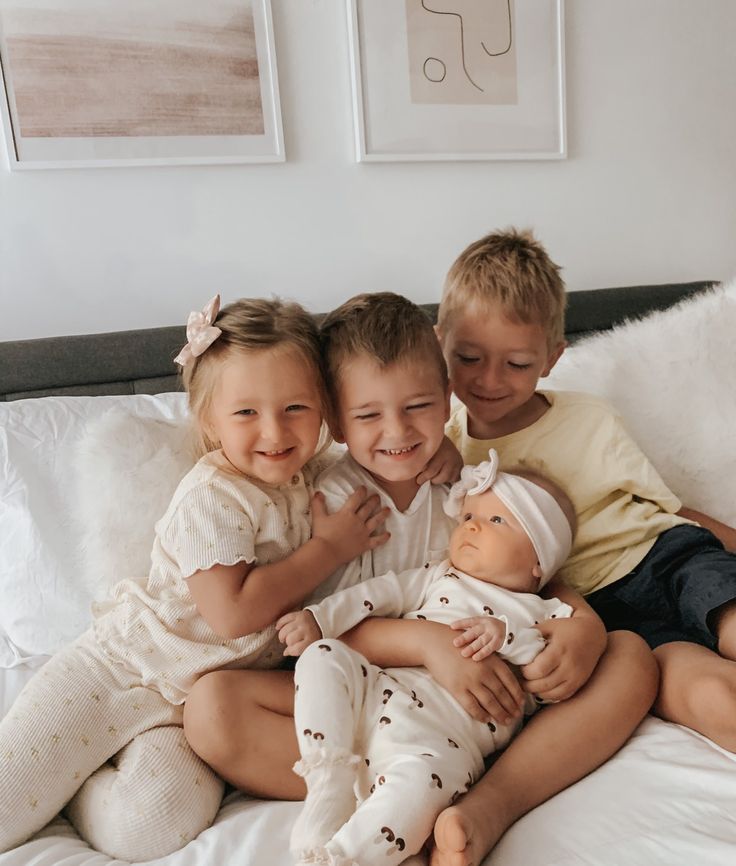 three children are sitting on a bed with their arms around each other and one is holding a doll