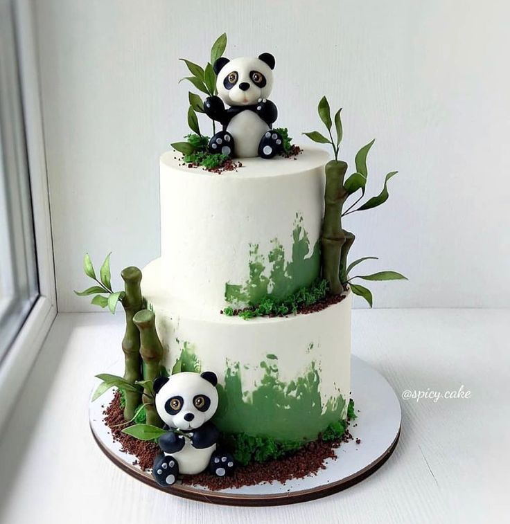 there is a three tier cake with panda bears on top and bamboo trees around it