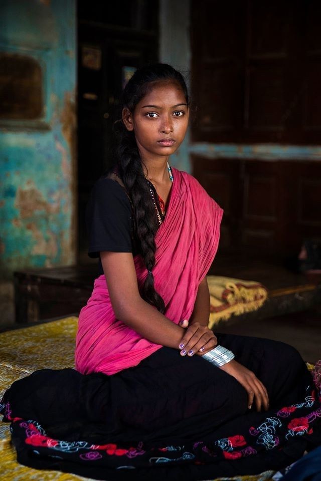 a woman sitting on top of a bed with a bottle in her hand and wearing a pink sari