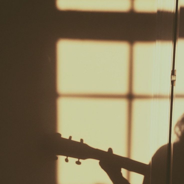a person holding a guitar in front of a window with the sun shining through it