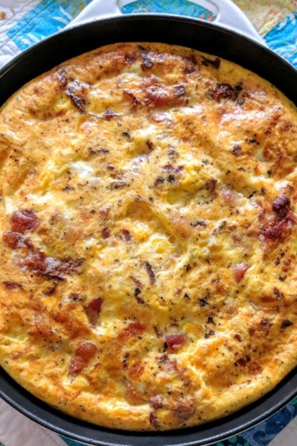 an omelet with bacon and cheese in a black pan on a blue table cloth