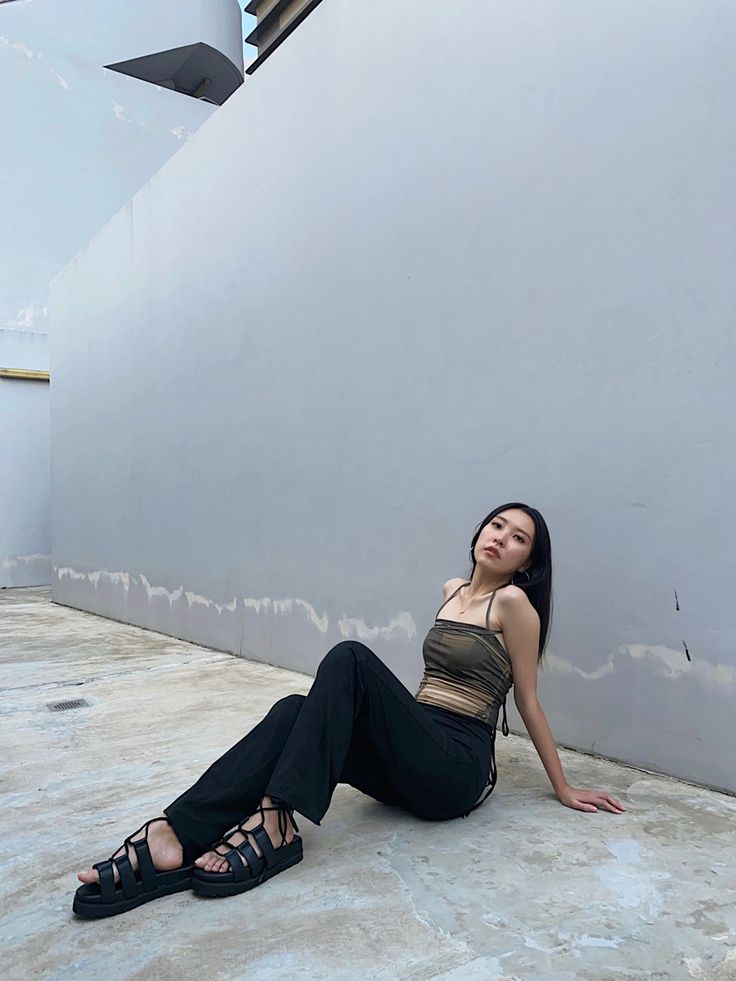 a woman sitting on the ground in front of a wall with her legs crossed out