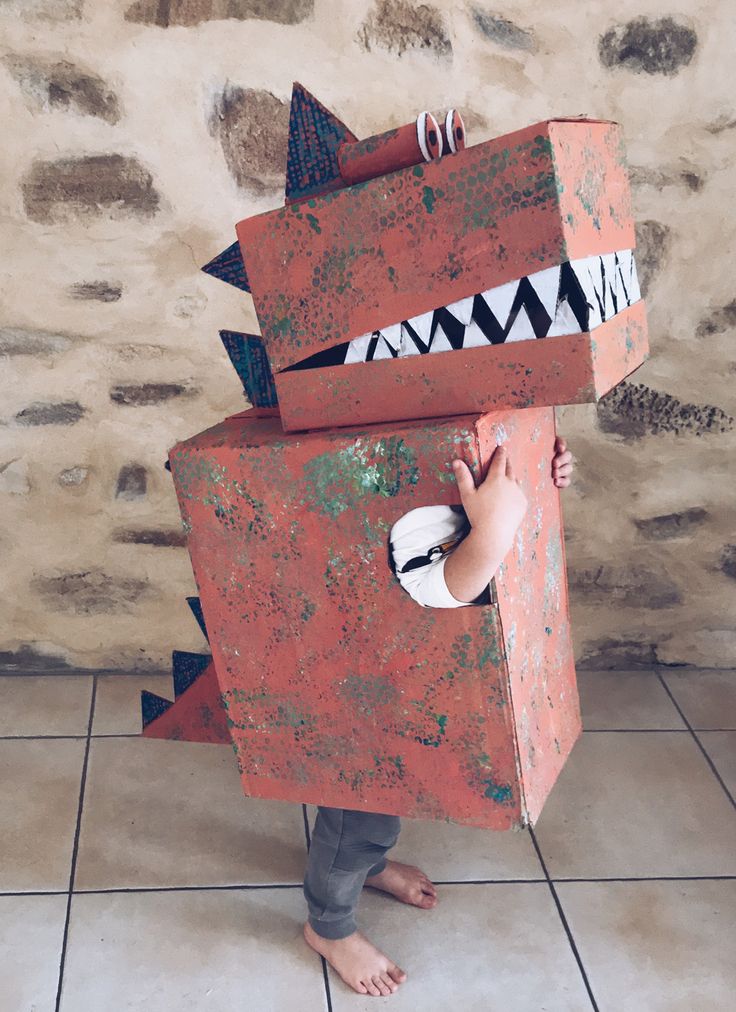 a young child is dressed up like a monster and has his hands on the back of an orange box