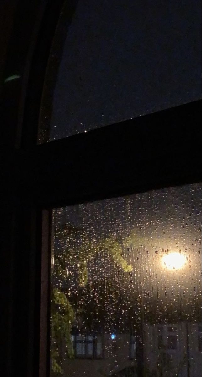 a window with rain drops on it and a street light in the background at night