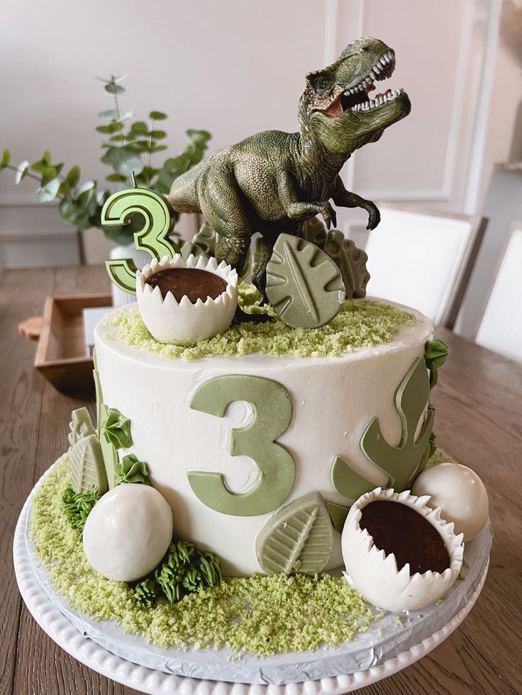 a dinosaur birthday cake is decorated with green and white decorations, including an egg shell