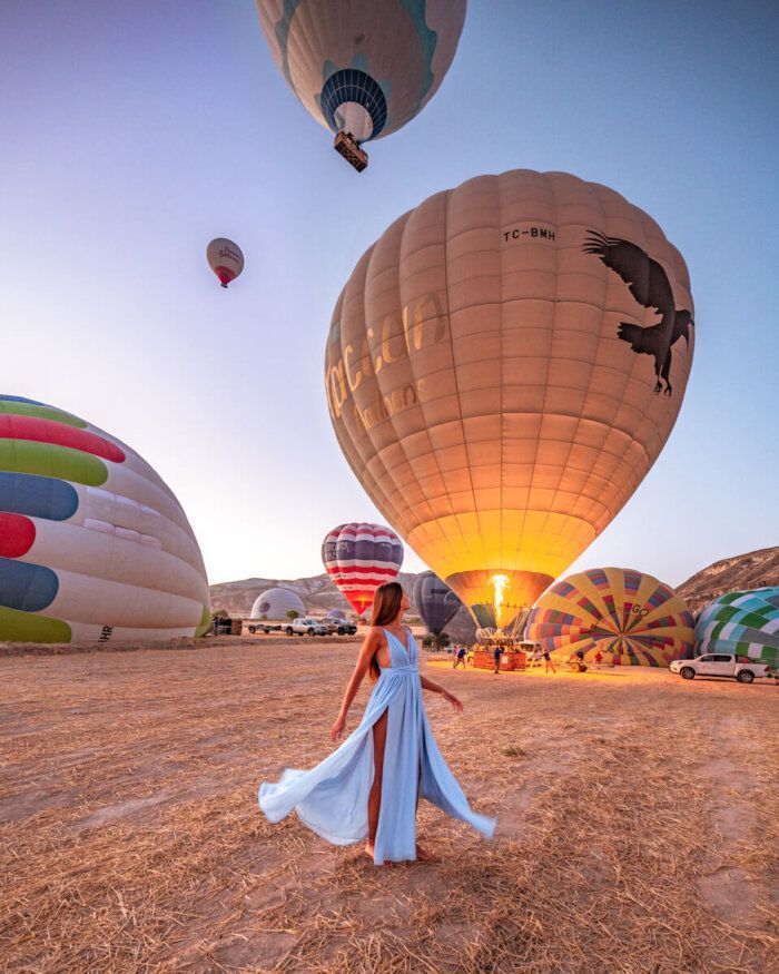 a woman in a blue dress is standing near hot air balloons that are being inflated