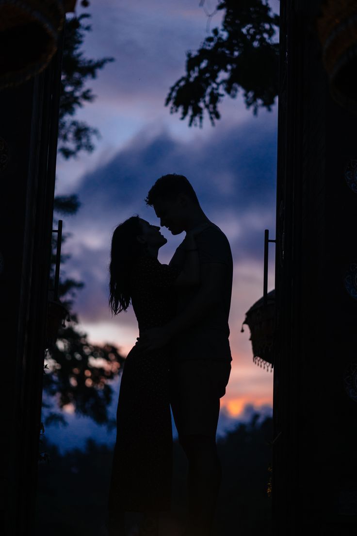 a man and woman standing next to each other in front of a window at sunset