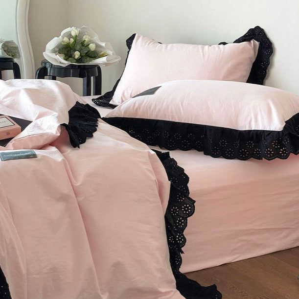 a bed with pink sheets and black ruffles on the bottom, along with two pillows