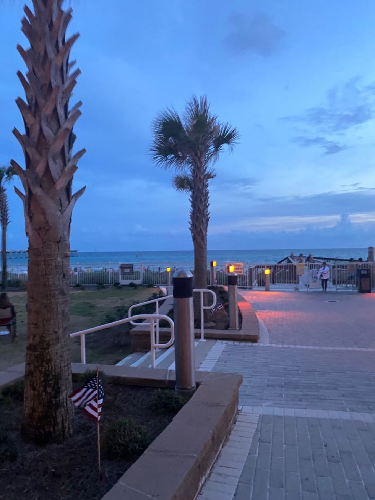 palm trees on the beach at dusk with an american flag in the foreground and boardwalk to the right