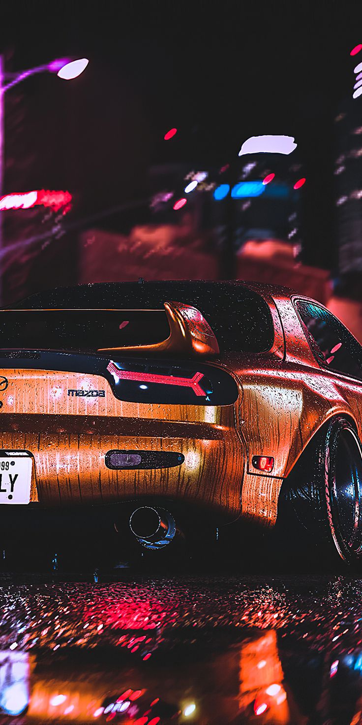 a car that is parked on the street in the rain with its hood up and it's lights reflecting off