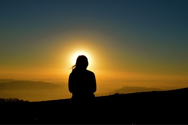 a person standing on top of a hill with the sun setting in the sky behind them