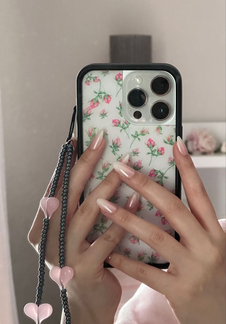 a woman holding up her phone case with pink flowers on it and hearts attached to the back