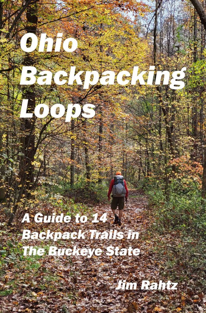 the back packer is walking down a trail in the woods with leaves on the ground