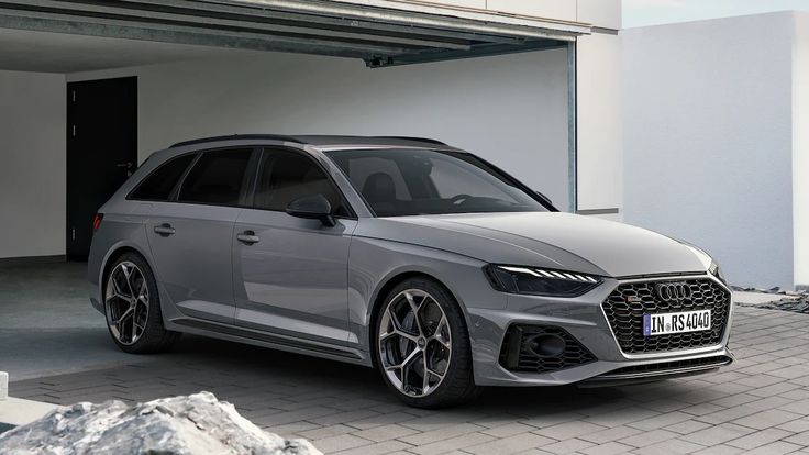 a grey car parked in front of a building with an open garage door next to it