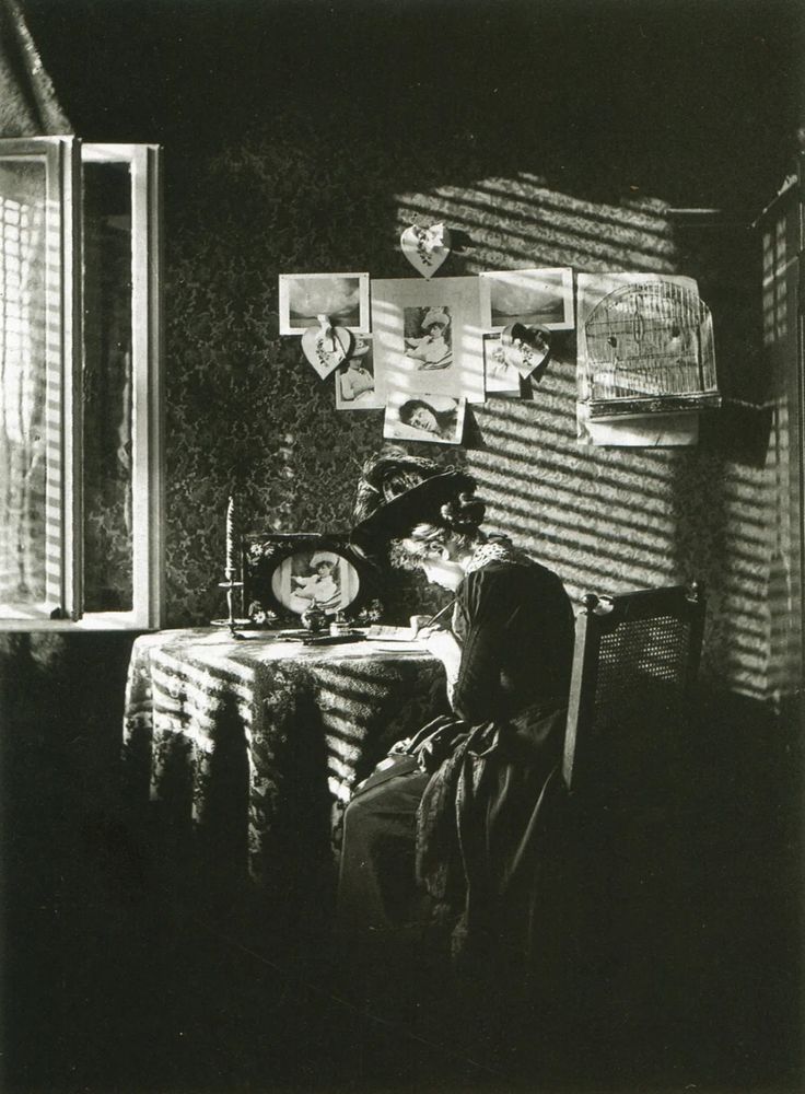 black and white photograph of a woman sitting at a table in front of a window