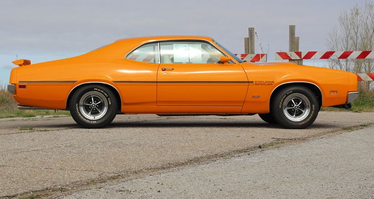 an orange car is parked on the side of the road in front of a barrier