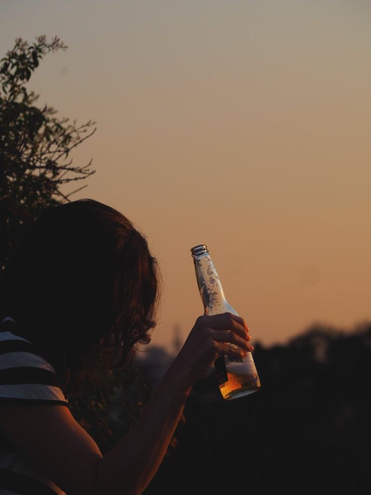 a woman holding a beer bottle at sunset