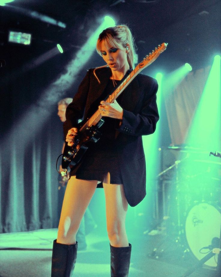 a woman in short shorts and knee high boots playing an electric guitar at a concert