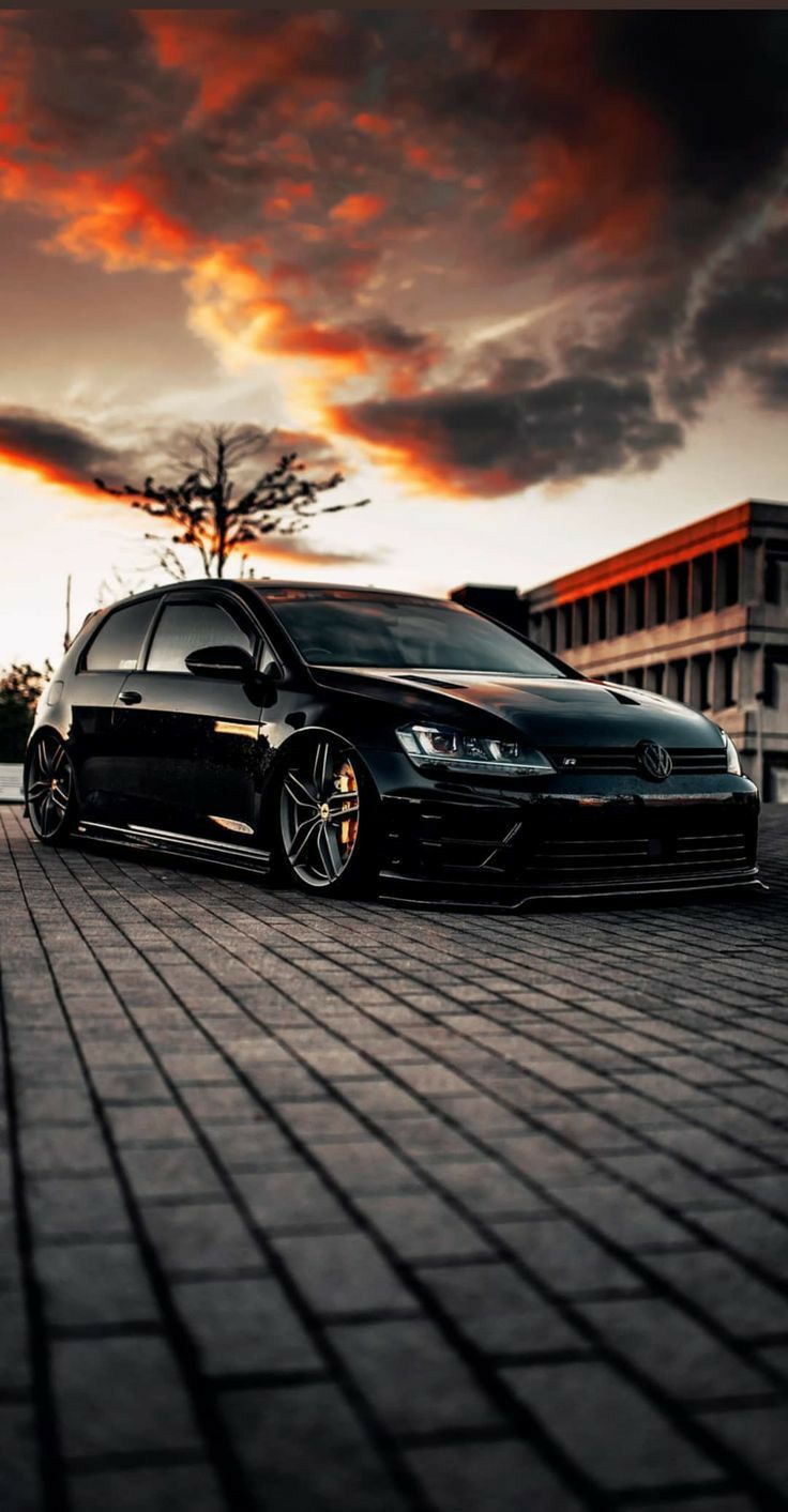 a black car parked on the side of a road next to a tall building at sunset