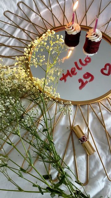 two cupcakes on a plate with candles and flowers in front of the sign