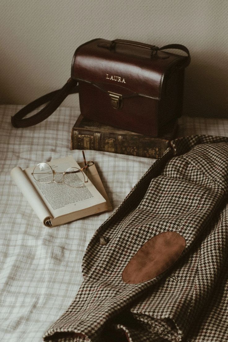 an open book sitting on top of a bed next to a purse and eyeglasses