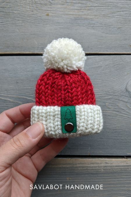 a hand holding a small knitted santa hat on top of a wooden table next to a piece of wood