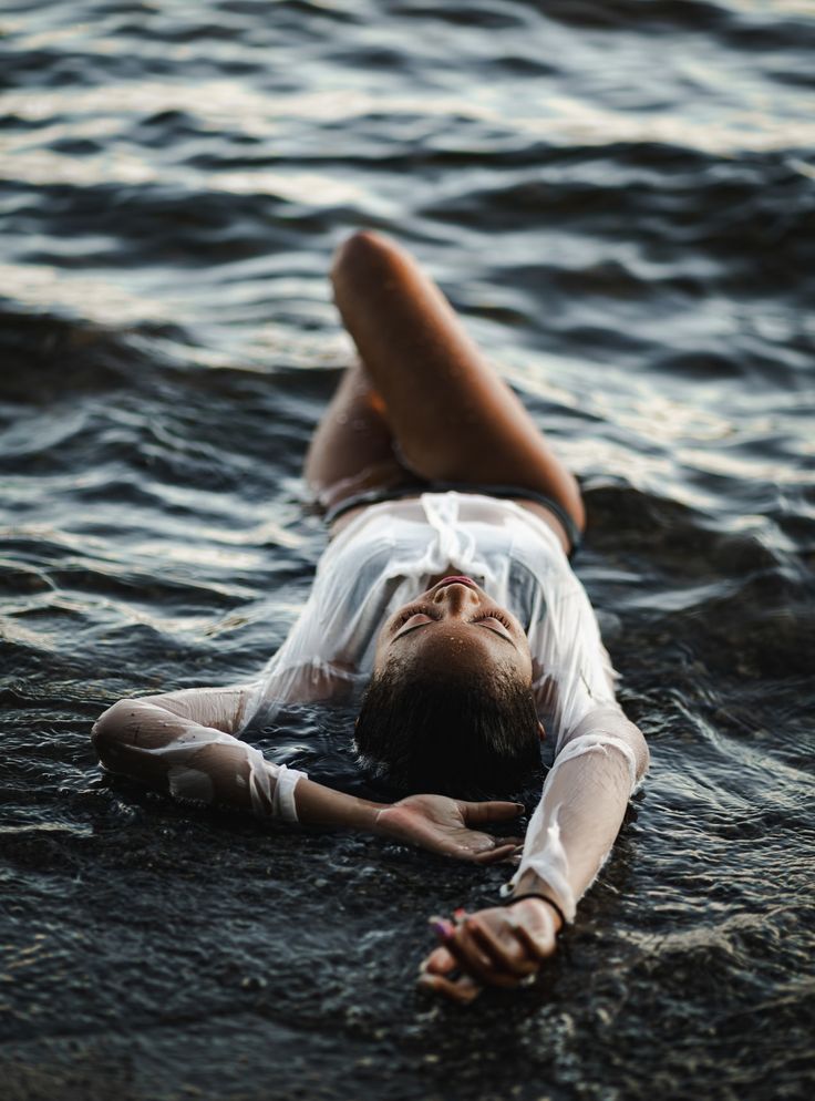 a woman laying on her back in the water wearing a white shirt and clear skirt