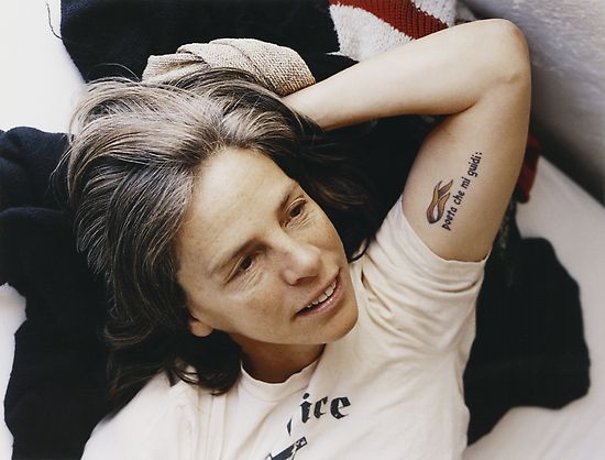 a woman laying on top of a bed next to a teddy bear and blanket with writing on her arm