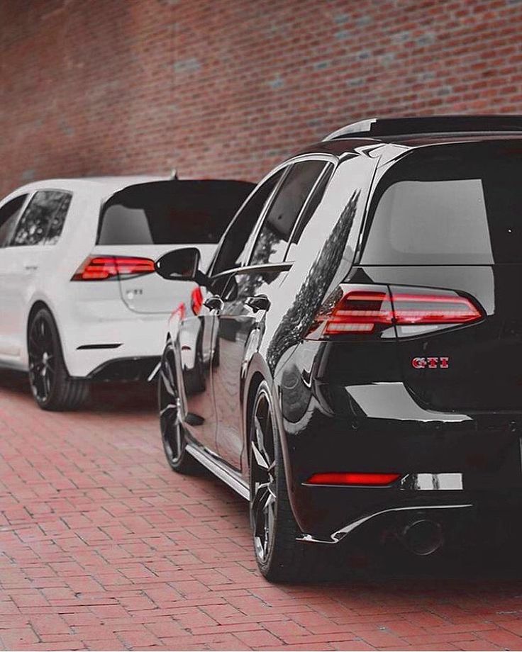 several cars parked on the side of a brick road in front of a red brick wall