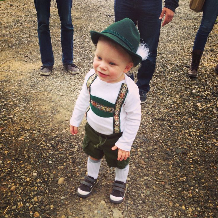 a small child wearing a green hat and suspenders standing in the dirt with other people