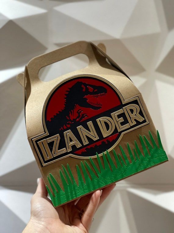 a hand holding up a cardboard box with an image of a dinosaur on it
