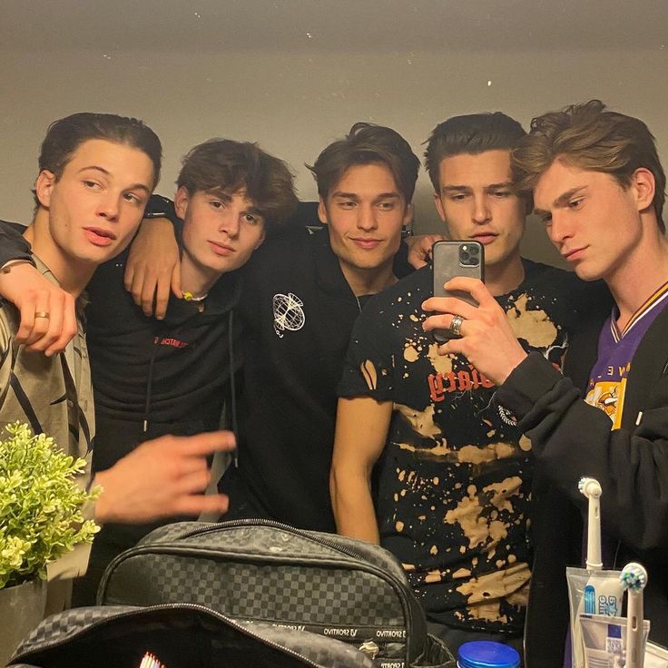a group of young men standing next to each other in front of a mirror taking a selfie