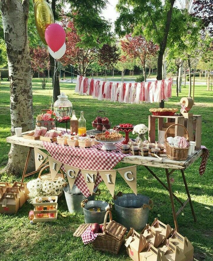 a picnic table with food and drinks on it in the middle of a park area