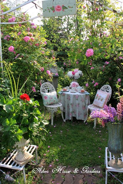 an outdoor table and chairs in the middle of a garden with pink flowers on it