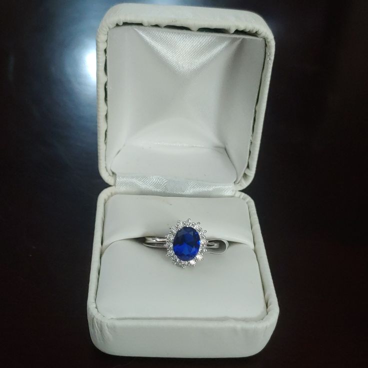 a ring with a blue stone sits in a white box on a black table top