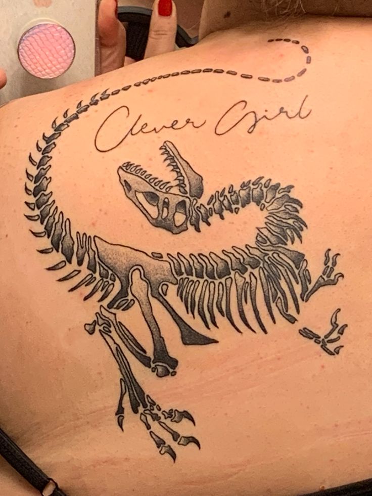 a woman with a tattoo on her back that has a dinosaur skeleton in the middle