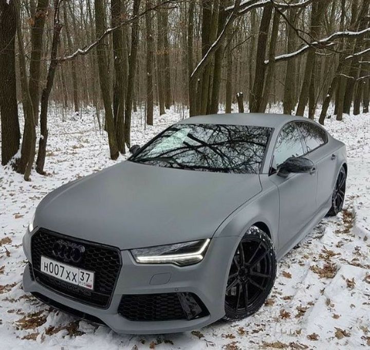 a grey car is parked in the snow near some trees and bushes with no leaves on it